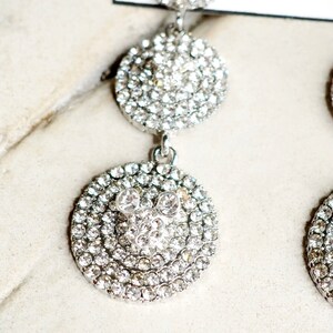May include: Silver dangle earrings with three round crystal-encrusted charms. The bottom charm features a Mickey Mouse silhouette.