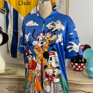 May include: A blue cycling jersey with a print of Mickey Mouse, Donald Duck, Goofy, and Pluto riding bicycles. The jersey has a zipper and the text "Mickey's Bicycle Club" and "Look Ma, No Hands!" printed on it.