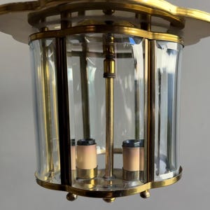 Może przedstawiać: Lampa sufitowa wykonana z mosiądzu i szkła o geometrycznym wzorze. Lampa ma przezroczysty klosz ze szkła z ozdobnym wzorem i trzy żarówki.