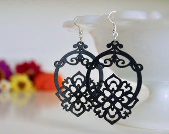 May include: A pair of black dangle earrings with a delicate, intricate design. The earrings are made of wood and feature a circular shape with a floral pattern.