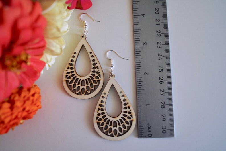 K&ouml;nnte beinhalten: Holz-Ohrringe in Tropfenform mit einem lasergeschnittenen Blumenmuster. Die Ohrringe sind etwa 7,6 cm lang und haben silberfarbene Ohrhaken. Die Ohrringe werden neben einem Lineal und bunten Blumen pr&auml;sentiert.