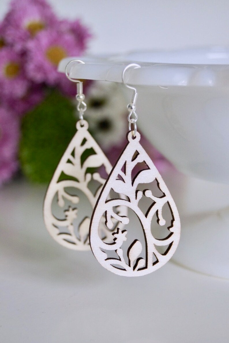May include: A pair of wooden earrings with a delicate floral design. The earrings are shaped like teardrops and have a natural wood finish.