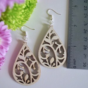 May include: A pair of wooden earrings with a teardrop shape and a delicate floral design. The earrings are approximately 5 cm long.