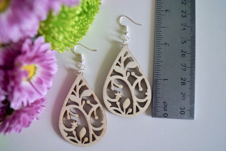 May include: A pair of wooden earrings with a teardrop shape and a delicate floral design. The earrings are approximately 5 cm long.