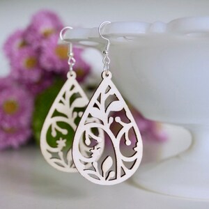 May include: A pair of wooden earrings with a teardrop shape and intricate floral cutouts. The earrings are made of light-coloured wood and have silver hooks.
