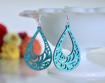 Pode incluir: Brincos de gota azul turquesa com um design floral recortado. Os brincos são feitos de madeira e têm ganchos prateados.