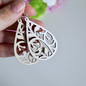May include: A pair of wooden earrings shaped like teardrops with a delicate floral cut-out design. The earrings are a light natural wood colour.