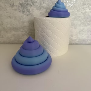 May include: Two whimsical, layered sculptures in shades of blue and purple, resembling stylized piles of poop, sit near a roll of white, patterned paper. The sculptures are on a white surface against a textured gray background.