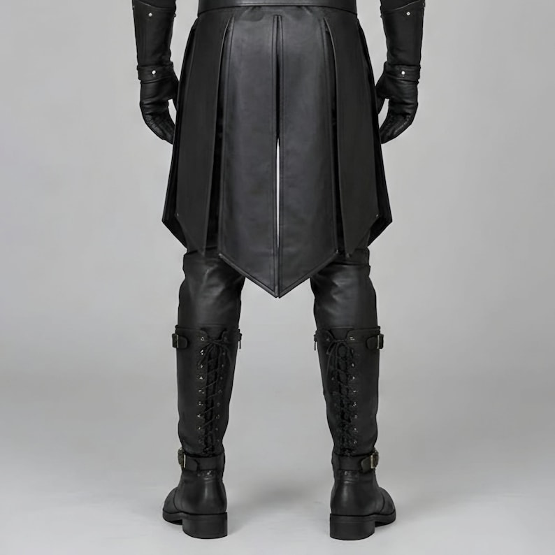 Front view of a man in a black leather wizard costume against a gray studio background. He wears a tall pointed hat, a fitted vest with silver clasps, and a long cloak with black fur trim around the collar and shoulders. Small silver rivets line the shoulder capelet and leather bracers. A buckle belt holds two long pointed waist panels over black trousers. Black gloves and tall boots complete the styling. The model faces forward with his arms relaxed, displaying the full outfit from head to toe.