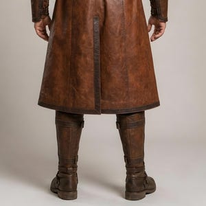Front and back views of a handmade men’s brown leather Viking coat costume featuring a long medieval warrior design, wide cream fur shoulder collar, lace-up front, metal buckle closures, waist belt, dark leather trim, fitted sleeves, wrist guards, split coat hem, matching brown trousers, and tall leather boots. Rustic fantasy outfit inspired by Norse styles, ideal for Viking cosplay, Renaissance fairs, LARP events, Halloween costumes, stage performances, themed parties, and fantasy photoshoots.