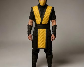 Puede incluir: Un disfraz negro y amarillo con capucha, máscara y chaleco acolchado. El disfraz incluye pantalones negros, botas y protectores de brazos. El chaleco amarillo tiene un patrón de diamantes. La persona está de pie frente a un fondo gris.