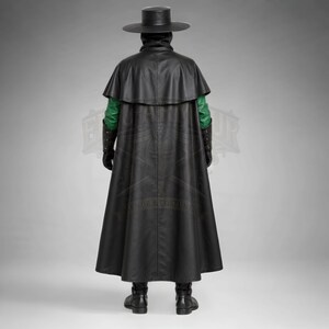 Man wearing a green leather plague doctor costume with a long lace-up coat, black buckle belt and flowing black cloak. A shoulder capelet frames the upper body, while quilted black bracers cover the forearms. The outfit is styled with black gloves, leg guards, boots, a wide-brimmed hat and a beaked mask with round eyepieces. He holds edge of the cloak and stands against a plain gray background. The vivid green coat contrasts with the black accessories, showing the costume's gothic fantasy style.