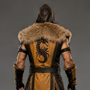 Black leather Viking ninja armor costume with antique gold leather panels, fur-trimmed shoulders, deep hood, adjustable waist belt, layered front armor, matching leather arm bracers, wrist guards and lower leg armor. Handmade medieval fantasy outfit with a rugged warrior-inspired design, suitable for Halloween, LARP, cosplay, Renaissance fairs, conventions, themed parties and fantasy photoshoots. Custom sizing and color options available.