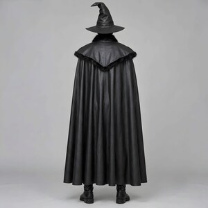 Front view of a man in a black leather wizard costume against a gray studio background. He wears a tall pointed hat, a fitted vest with silver clasps, and a long cloak with black fur trim around the collar and shoulders. Small silver rivets line the shoulder capelet and leather bracers. A buckle belt holds two long pointed waist panels over black trousers. Black gloves and tall boots complete the styling. The model faces forward with his arms relaxed, displaying the full outfit from head to toe.
