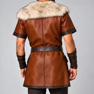 Men’s Viking leather tunic costume in brown leather with a wide fur shoulder collar, dark brown trim, adjustable buckle closures, waist belt, utility pouches, and matching leather forearm bracers. Front and back views show the knee-length Norse warrior tunic with short sleeves, fur across the shoulders, fitted belt, and medieval detailing. Ideal for Viking cosplay, LARP, Renaissance fairs, Halloween, fantasy events, and Norse warrior costumes.