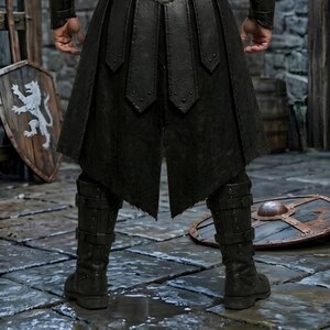 Men’s black Viking leather armor costume with layered chest panels, dramatic black fur shoulder trim, double buckle waist belts, segmented leather battle skirt, matching forearm bracers, and black leg armor. Full front view shows a dark Norse warrior outfit with structured leather detailing and rugged medieval styling. Ideal for Viking cosplay, medieval LARP, Renaissance fairs, Halloween, fantasy conventions, warrior costumes, stage events, and themed photoshoots.