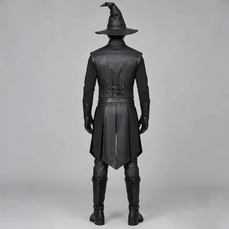Front view of a man in a black leather wizard costume against a gray studio background. He wears a tall pointed hat, a fitted vest with silver clasps, and a long cloak with black fur trim around the collar and shoulders. Small silver rivets line the shoulder capelet and leather bracers. A buckle belt holds two long pointed waist panels over black trousers. Black gloves and tall boots complete the styling. The model faces forward with his arms relaxed, displaying the full outfit from head to toe.
