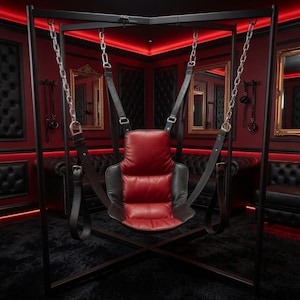 May include: A black metal frame supports a suspended seat featuring a red padded center and black leather sides. The seat is attached to the frame by four silver metal chains and adjustable black leather straps with buckles and loops.