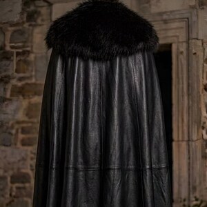 Men’s red and black Gothic vampire leather coat featuring a high standing collar, black fur-trimmed shoulders, double-breasted button detailing, wide waist belt, cross-body leather strap, long sleeves, and a dramatic floor-length silhouette. The dark Victorian-inspired design creates a Vampire Lord look ideal for Halloween, gothic cosplay, LARP, Renaissance fairs, masquerade events, fantasy conventions, stage performances, costume parties, and themed photoshoots.