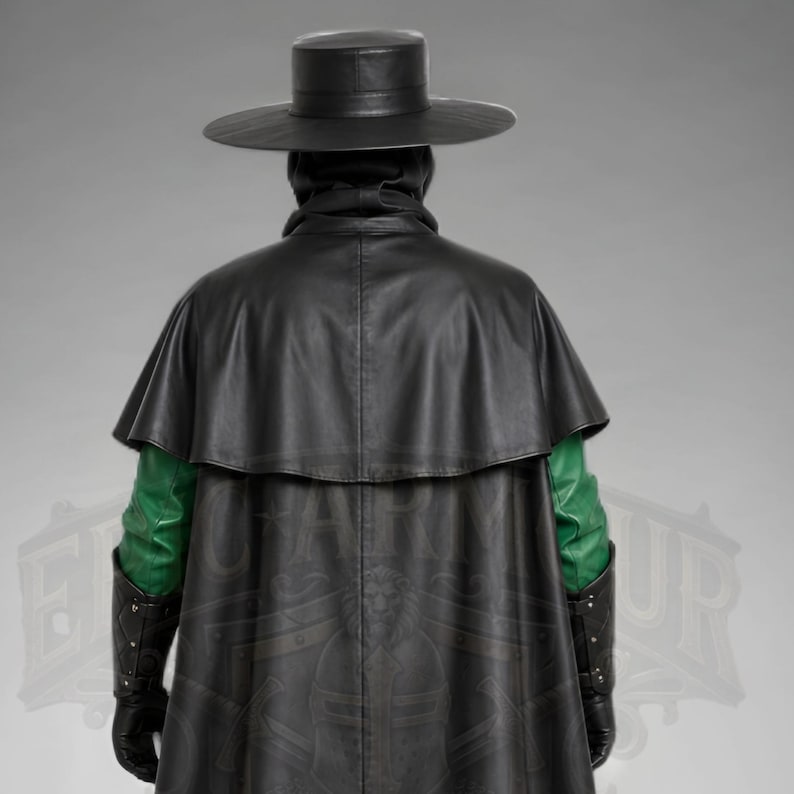 Man wearing a green leather plague doctor costume with a long lace-up coat, black buckle belt and flowing black cloak. A shoulder capelet frames the upper body, while quilted black bracers cover the forearms. The outfit is styled with black gloves, leg guards, boots, a wide-brimmed hat and a beaked mask with round eyepieces. He holds edge of the cloak and stands against a plain gray background. The vivid green coat contrasts with the black accessories, showing the costume's gothic fantasy style.