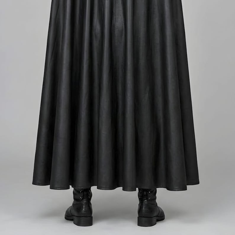 Front view of a man in a black leather wizard costume against a gray studio background. He wears a tall pointed hat, a fitted vest with silver clasps, and a long cloak with black fur trim around the collar and shoulders. Small silver rivets line the shoulder capelet and leather bracers. A buckle belt holds two long pointed waist panels over black trousers. Black gloves and tall boots complete the styling. The model faces forward with his arms relaxed, displaying the full outfit from head to toe.