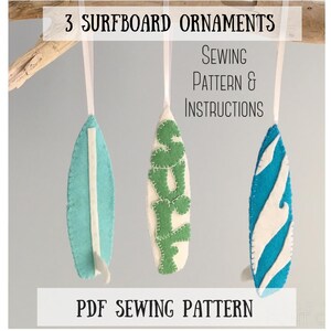 May include: Three felt surfboard ornaments hanging from ribbons. The left is light blue with a white stripe, the center is white with green felt letters spelling SURF, and the right is blue and white striped. Text reads 3 SURFBOARD ORNAMENTS.