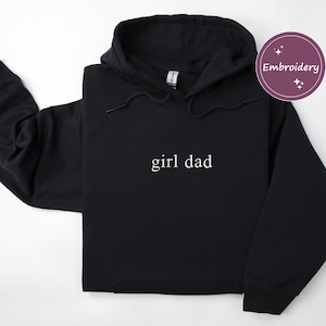 Puede incluir: Sudadera con capucha negra con la frase "girl dad" en blanco. La sudadera tiene una capucha con cord&oacute;n y mangas largas. La palabra "Embroidery" est&aacute; en un c&iacute;rculo morado en la esquina superior derecha.