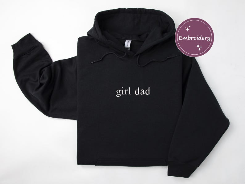 Puede incluir: Sudadera con capucha negra con la frase "girl dad" en blanco. La sudadera tiene una capucha con cord&oacute;n y mangas largas. La palabra "Embroidery" est&aacute; en un c&iacute;rculo morado en la esquina superior derecha.