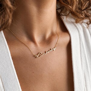 Può includere: Una collana in metallo color oro con una catenina sottile e un ciondolo centrale. Il ciondolo riporta il nome Kimberly scritto in un carattere corsivo fluido e continuo, sospeso a una sottile catena a maglie lucide.