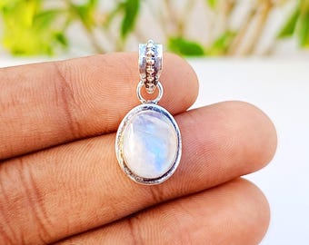 May include: Oval-shaped pendant with a moonstone center and a silver-colored metal setting. The moonstone has a milky white and blue iridescent appearance. The pendant is suspended from a small, decorative bail.