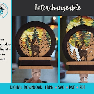 May include: A wooden nightlight with a deer and forest scene, featuring a 3.5-inch insert. The design includes a circular frame with a deer silhouette and trees, set against a colorful backdrop. The base is light-colored wood.