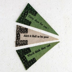 May include: Three triangular paper pennants with black and white patterned borders and black text. The text on the pennants reads: "Thirty days for you", "Ain't it Hell to be poor", and "Who'd think they cud".