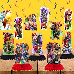 May include: A collection of colorful Street Fighter-themed party decorations. Each decoration features a character illustration with a "VS" logo. The decorations are on a wooden surface with a yellow background and decorative streamers.