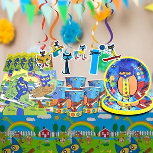 May include: A colorful party supplies set featuring a blue cat theme. Includes plates, cups, napkins, and decorations. The plates and cups have a cartoon cat design. The table cover has a rainbow and dinosaur pattern.