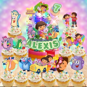 May include: A colorful birthday cake and cupcakes featuring Dora the Explorer characters. The cake has a rainbow-layered design with a topper that says "Happy Birthday" and the name "Alexis". Cupcakes are decorated with Dora-themed toppers.