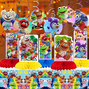 May include: A colorful party decoration set featuring various Muppet characters. The set includes circular cutouts and rectangular centerpieces with images of Kermit, Fozzie Bear, and other Muppet Show characters. The table is decorated with honeycomb centerpieces.