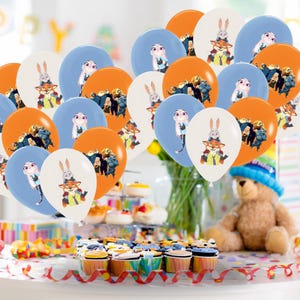 May include: A selection of orange, blue, and white balloons, each printed with cartoon characters. The balloons are arranged to create a celebratory atmosphere. Cupcakes and a teddy bear are also visible, suggesting a party or event.