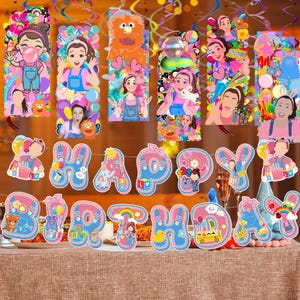 May include: A festive birthday party banner and hanging decorations. The banner spells out "HAPPY BIRTHDAY" in blue and pink letters with various cartoon illustrations. The hanging decorations feature cartoon characters and colorful streamers.