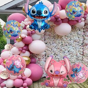 Puede incluir: Un arreglo festivo de globos rosas, blancos y dorados, con varios globos de aluminio con forma de personajes. Los globos presentan al personaje Stitch, en azul y rosa. El fondo incluye una pared floral.