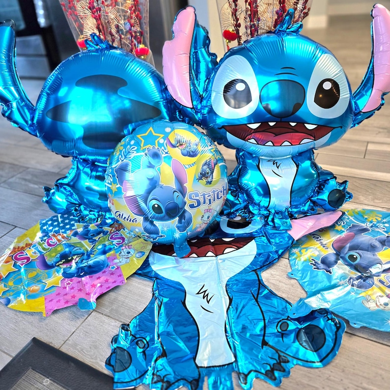 May include: A collection of blue foil balloons in the shape of the character Stitch. The balloons include a large Stitch head, a Stitch body, and smaller round balloons with Stitch graphics. Pink accents are visible on the ears and other areas.