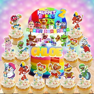 May include: A colorful birthday cake and cupcakes featuring Muppet Babies characters. The cake is rainbow-layered with the name "Chloe" and a "Happy Birthday" banner. Cupcakes are topped with frosting, sprinkles, and character toppers. The image has a Disney Muppet Babies theme.