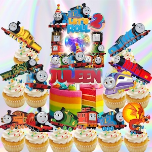 May include: A colorful birthday cake and cupcakes featuring Thomas the Tank Engine characters. The cake has rainbow layers and the name "Juleen". Cupcakes are topped with white frosting and train decorations. The cake topper says "Let's Roll" and the number "2".