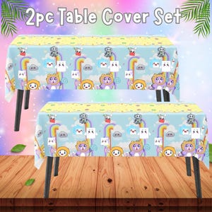 May include: Two-piece table cover set. The covers feature a light blue background with cartoon characters, rainbows, and clouds. The top border is yellow. The text "2pc Table Cover Set" is at the top.