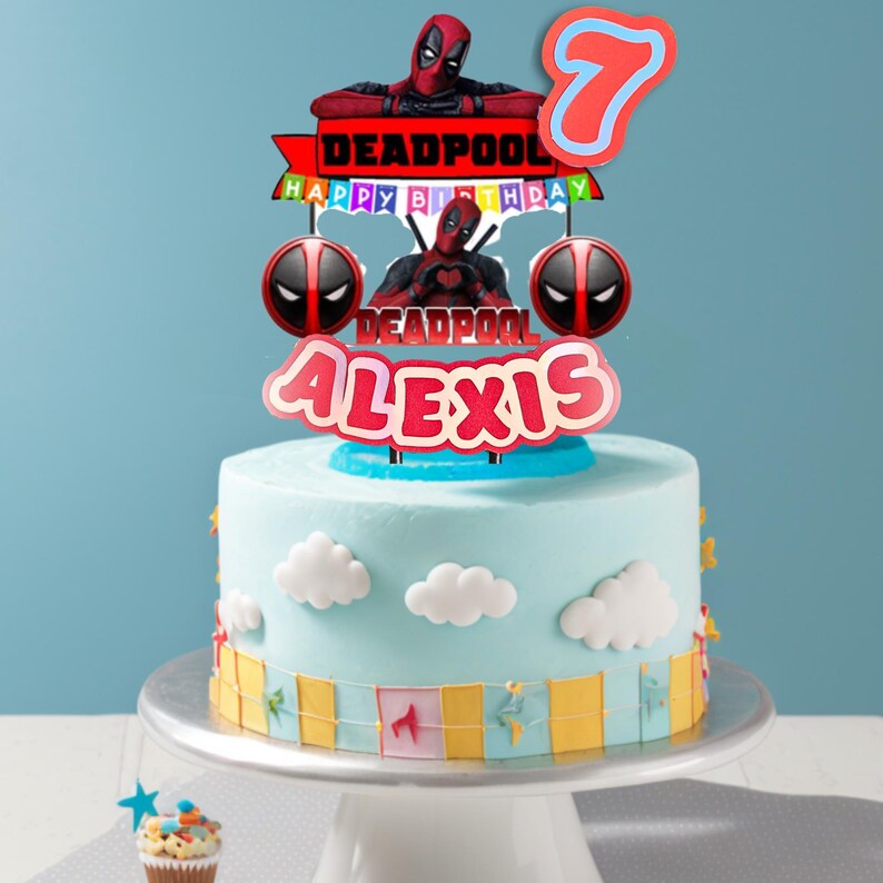 Puede incluir: Un pastel azul claro decorado con detalles de nubes blancas y un adorno tem&aacute;tico de Deadpool. El adorno incluye el nombre "Alexis", el n&uacute;mero "7" y las palabras "Happy Birthday". El pastel est&aacute; sobre un soporte blanco.