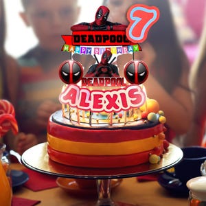 Puede incluir: Una colorida tarta de cumplea&ntilde;os con tem&aacute;tica de Deadpool. La tarta tiene capas rojas, amarillas y naranjas, coronada con una figura de Deadpool, el n&uacute;mero 7 y el nombre "Alexis". Est&aacute; decorada con logotipos de Deadpool y la frase "Happy Birthday".