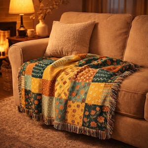 May include: A patchwork throw blanket with a fringed edge is draped over a beige sofa. The blanket features a variety of square patterns in shades of yellow, orange, and teal, creating a cosy and inviting aesthetic.