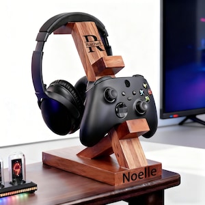 May include: A wooden gaming headset and controller stand with personalized engraving. The stand is made of dark wood and features a black headset and controller. The stand is engraved with the name "Rachel" and "Noelle".