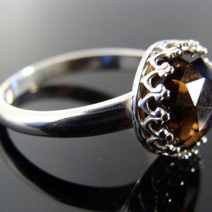 Puede incluir: Un anillo de plata con una gran piedra preciosa marr&oacute;n facetada engastada en un engaste en forma de corona.