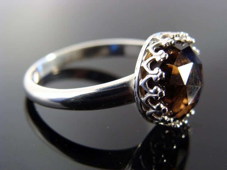 Puede incluir: Un anillo de plata con una gran piedra preciosa marr&oacute;n facetada engastada en un engaste en forma de corona.