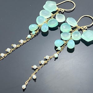 May include: Elegant gold-tone earrings featuring clusters of light blue and clear gemstones. The earrings have a cascading design with various shapes of gemstones, including teardrops and faceted stones, suspended from delicate chains.